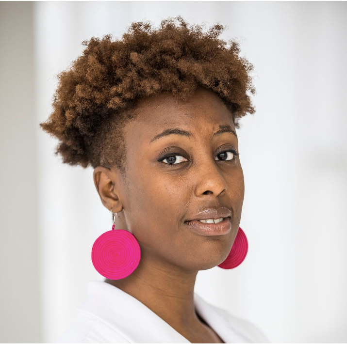 Vanessa Thomas, a Black woman looks towards the camera. She has bright pink earrings on and a white shirt.