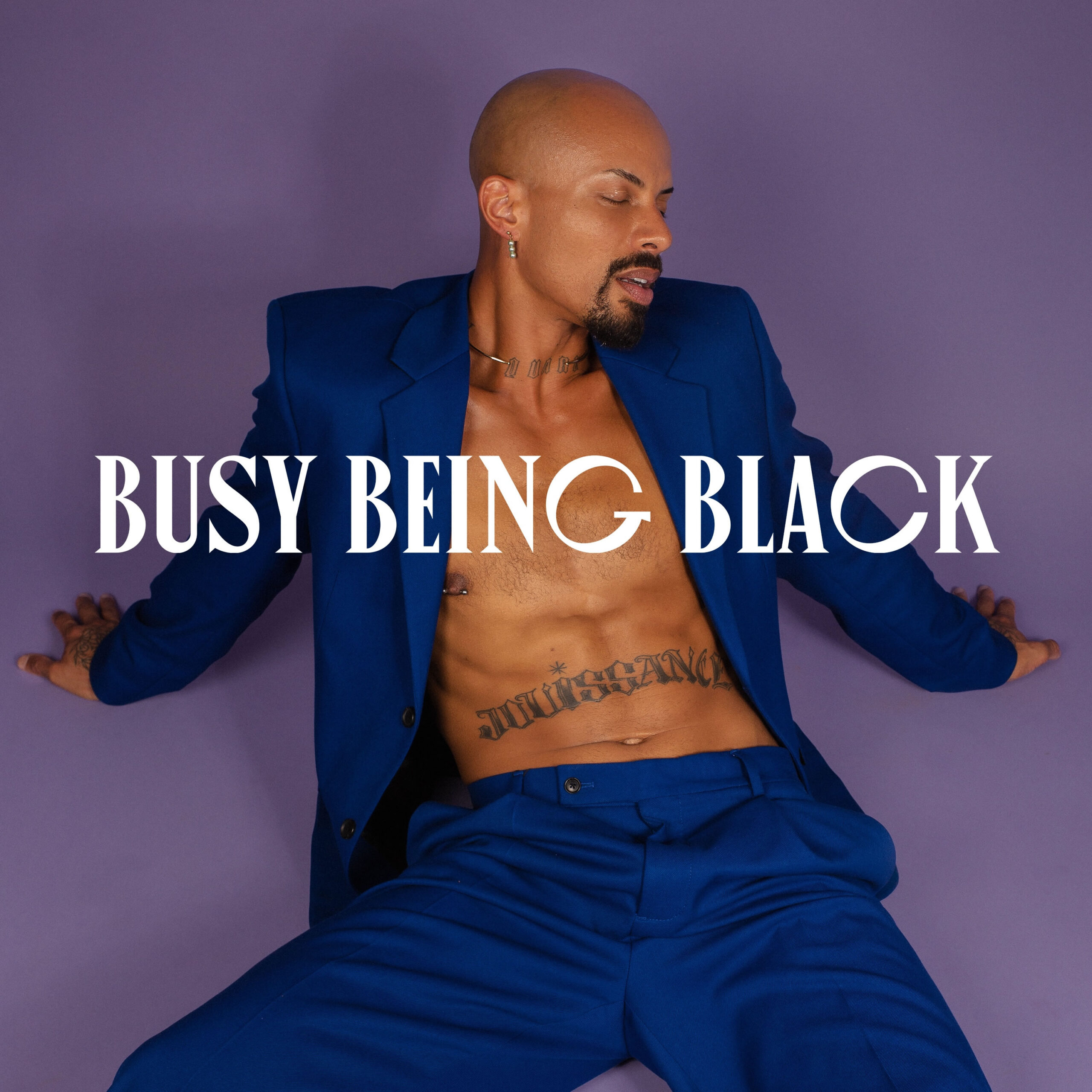 Josh rivers in a blue suit with no shirt sitting down and looking to the left with a purple background. Text on top reads Busy Being Black